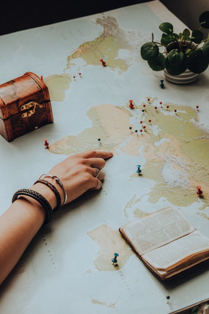 Hand pointing on a world map surrounded by travel essentials, sparking a sense of adventure.