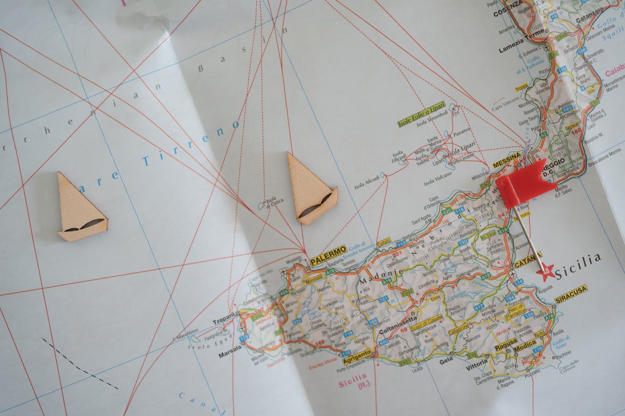 Travel planning concept featuring a Sicily map with wooden boat markers and a red pin.